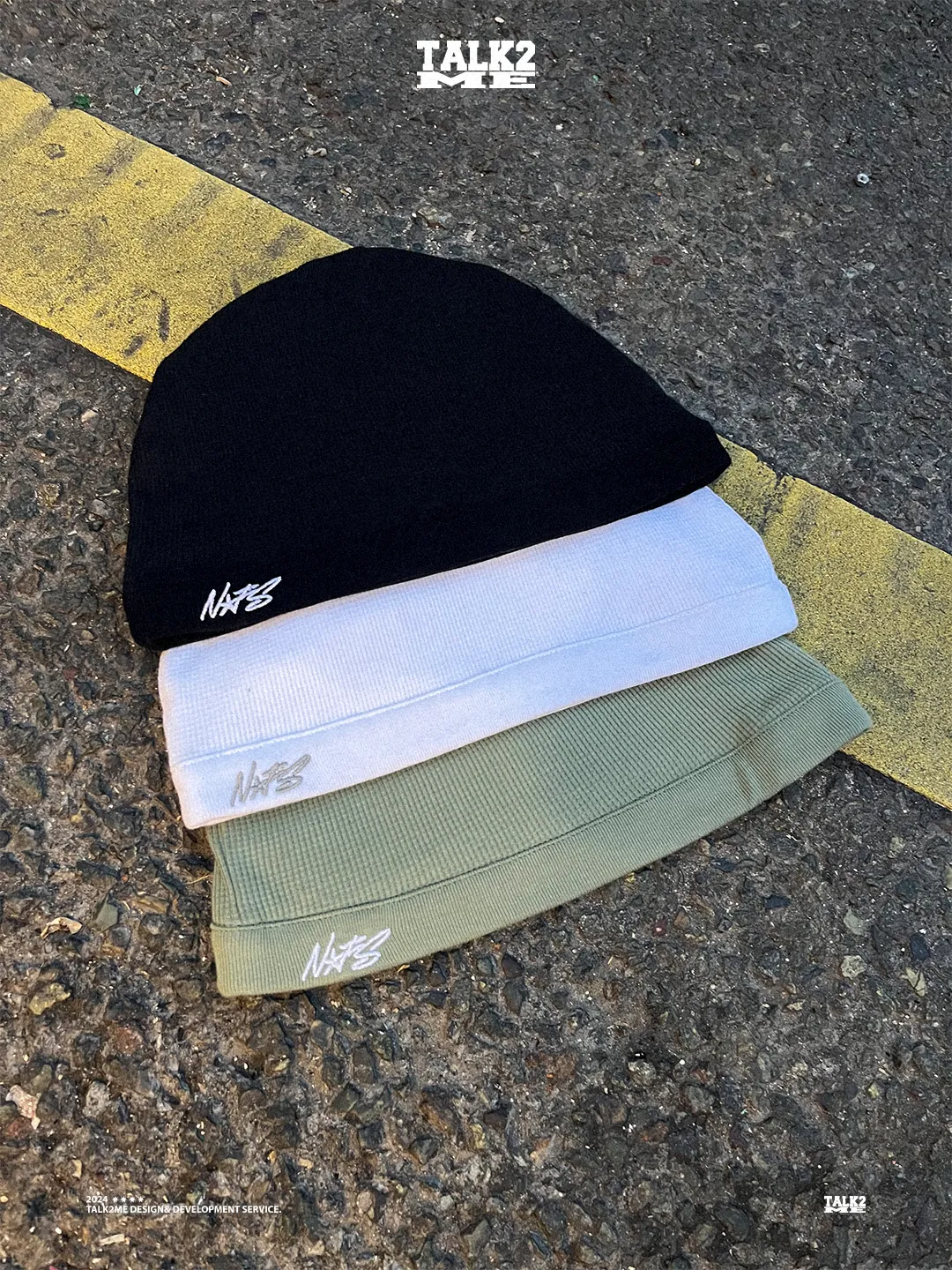 Content-Talks-Studio: drei Beanies mit Stick-Logo auf Asphalt mit gelber Fahrbahnmarkierung.